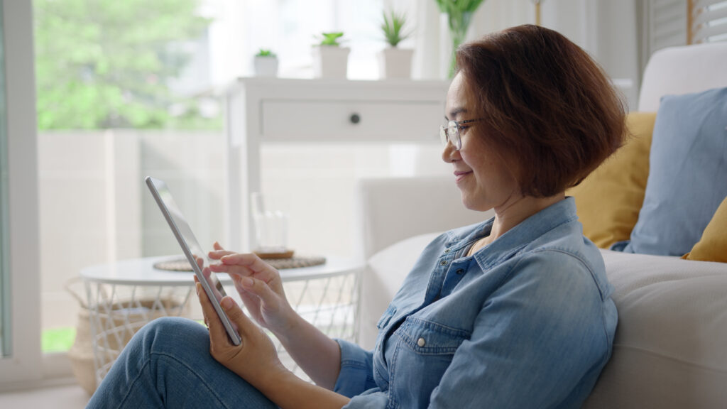 A lady sitting and relaxing at home on a sofa couch using a digital tablet looking at an accessible website.